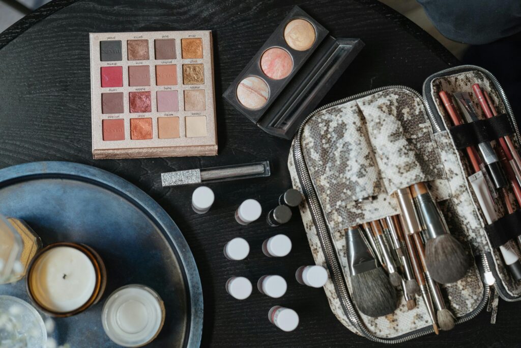 High-angle shot of cosmetics including brushes and an eyeshadow palette on a dark surface.